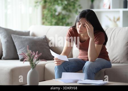 Worried asian woman checking bill sitting on a sofa at home Stock Photo