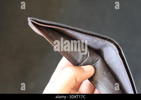 Close-up of Hand Holding an Empty Black Leather Wallet: Concept of Financial Crisis, Poverty, and Running Out of Cash on a Dark Background Stock Photo