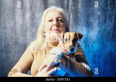 Jack Russell dog with white and brown fur in his owner's arms. The two are photographed on a dark background Stock Photo