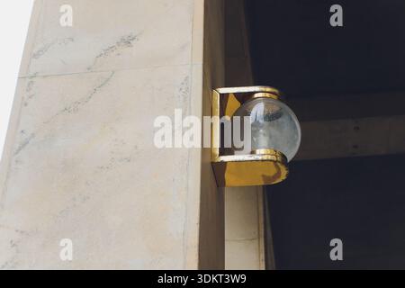 Contemporary wall mount glow. Modern vintage fixture casting gentle shadows on wall. Stylish brass lamp adorns concrete exterior with inviting ambient Stock Photo
