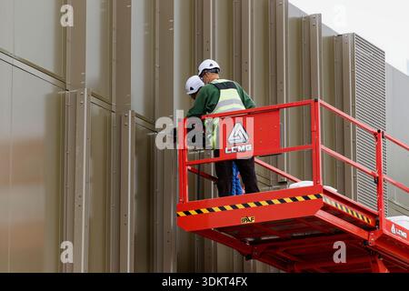 Two contractors with ppe on scissor lift fitting aluminium fins to ...