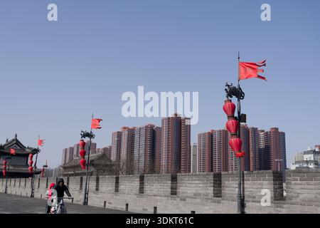 Tandem bike riding along the Xi'an city wall, red lantern poles in the foreground and modern residential towers in the background Stock Photo