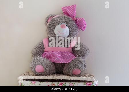 Tedwina Bear Cute female teddy bear soft cuddly toy wearing pink polka dot dress and matching bow sitting on wicker basket Stock Photo