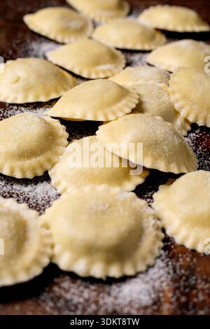 Fresh homemade ravioli pasta scattered with flour on wooden cutting board. Traditional Italian cuisine preparation process. Stock Photo