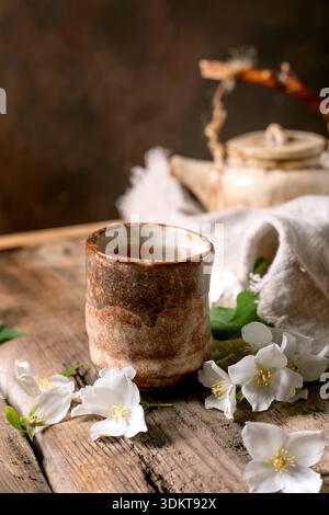 Ceramic tea cup with hot tea white spring flowers teapot on wooden table. Traditional oriental tea ceremony setup with natural decoration. Stock Photo