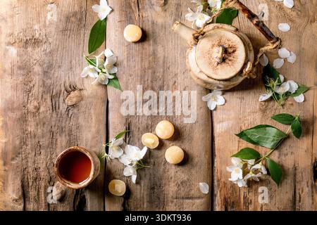 Traditional tea set with glass teapot and cup on rustic wooden table decorated with white jasmine flowers and mochi balls top view Stock Photo