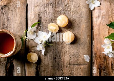 Ceramic tea cup on rustic wooden table decorated with white jasmine flowers and traditional asian sweets mochi balls top view Stock Photo