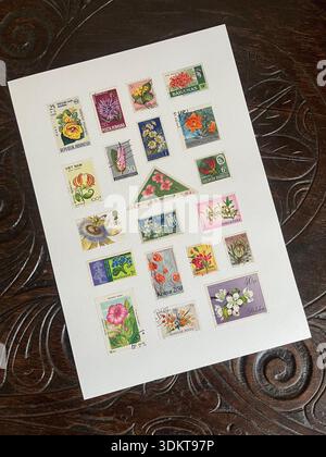 A collection of vintage postage stamps featuring plants and flowers on a decorative oak table top. Stock Photo