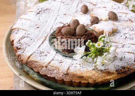 Homemade Easter cake Pastiera Napolitano dusted with powdered sugar decorated with chocolate nest containing small chocolate eggs and white spring flo Stock Photo