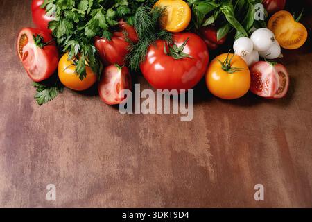 Fresh colorful tomatoes herbs mushrooms arranged on rustic wooden surface. Ingredients for healthy cooking salads Mediterranean cuisine. Stock Photo