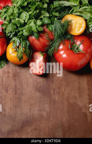 Red ripe tomatoes with fresh green herbs cilantro basil dill arranged on rustic wooden background. Healthy organic vegetables for cooking Stock Photo