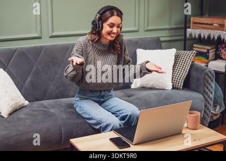 Woman having a joyful conversation on her laptop, sharing laughs and staying connected through the internet from the comfort of her home. Stock Photo