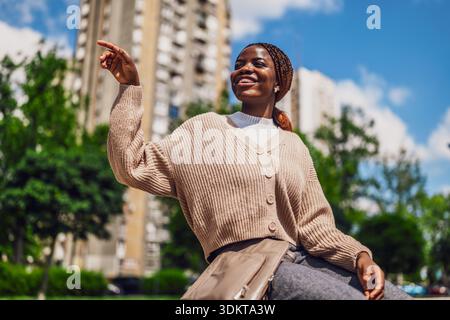 Outdoor portrait of happy Black woman who is sitting outdoor on sunny day and enjoying herself. Stock Photo