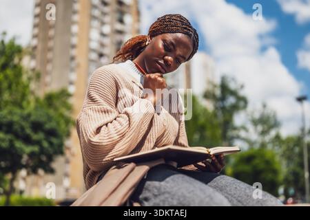 African American woman relaxing in the city park, deep in thought and she is writing her diary. Stock Photo
