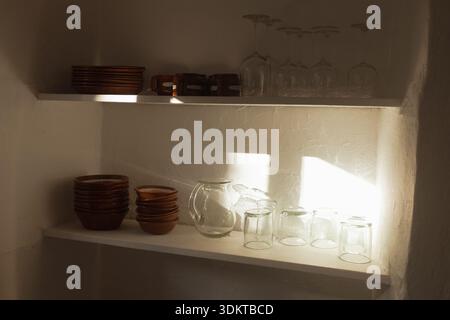 Kitchen shelves storing pottery and glassware in sunlight Stock Photo