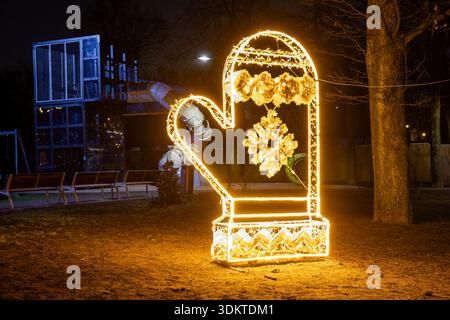 A large mitten shaped decoration lit with yellow lights in a park at night, with a playground, trees, and a faint moon visible in the background. Stock Photo