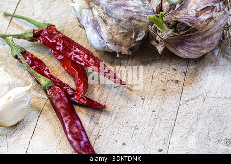 A bunch of red peppers and garlic on a wooden table. The peppers are dried and the garlic is fresh Stock Photo
