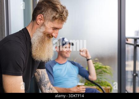 Two male friends having drinks and laughs on city balcony Stock Photo