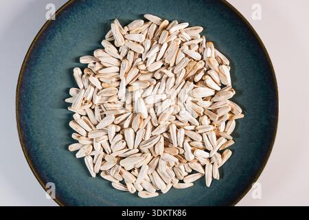 Light beige sunflower seeds with brown streaks form a circular pattern on a textured dark teal plate, set against a plain white background. Stock Photo