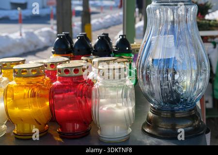 Glass grave candles in red, yellow and white arranged outdoors on a table beside a large blue lantern. Stock Photo