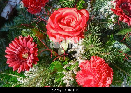 Artificial red flowers and evergreen branches arranged outdoors in winter. Stock Photo