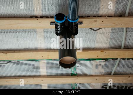 Ceiling view of house under construction featuring black and blue ducts of a recuperation ventilation system mounted on wooden beams. Stock Photo