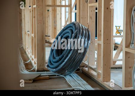 Interior view of a house under construction featuring wooden framing, exposed wiring, and a coiled ventilation duct on the floor under natural light. Stock Photo