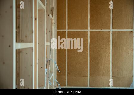 Interior view of a house under construction featuring wooden framing, insulation panels, and visible electrical wiring in an unfinished state. Stock Photo