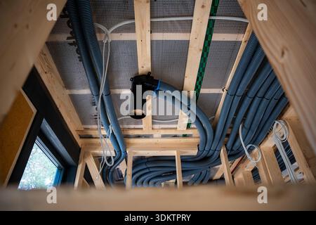 Interior view of a house under construction featuring wooden beams, blue ventilation ducts, a black outlet, electrical wiring, and natural light from Stock Photo