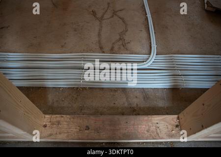 New house construction site featuring white ventilation ducts on a concrete floor, wooden framing in the foreground, and visible construction debris. Stock Photo