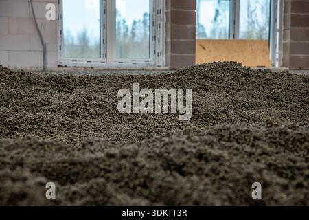 Construction site interior featuring gravel on the floor, concrete block walls, large window openings, and a wooden board leaning against a frame. Stock Photo