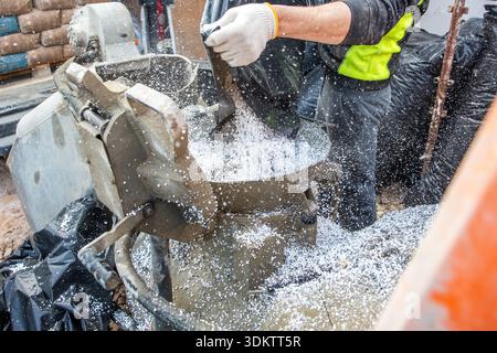 A worker in high visibility gear pours white granules into a concrete mixer surrounded by black coverings and construction materials at an active site Stock Photo