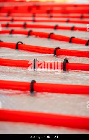 Bright red underfloor heating pipes arranged in parallel lines, secured with black clips on a metallic reflective surface during a heating system inst Stock Photo