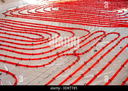 Bright red underfloor heating pipes secured with black clips on a silver reflective surface, prepared for concrete application in a construction proje Stock Photo