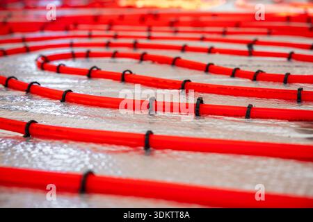 Red underfloor heating pipes arranged in a curved pattern, secured with black clips on a reflective surface, prepared for Estrich concrete application Stock Photo