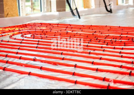 Bright red underfloor heating pipes arranged in loops over reflective insulation, secured with black fasteners, in a well lit construction site interi Stock Photo