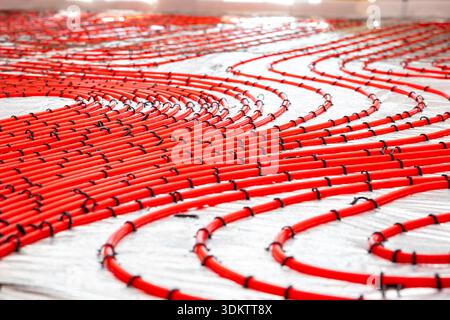 Red underfloor heating pipes arranged in curved patterns, secured with black clips on a light surface, prepared for Estrich concrete application. Stock Photo
