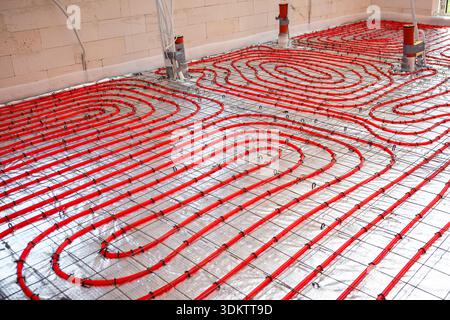 Interior of a construction site showing red underfloor heating pipes arranged in a spiral pattern on a metallic mesh over reflective insulation. Stock Photo