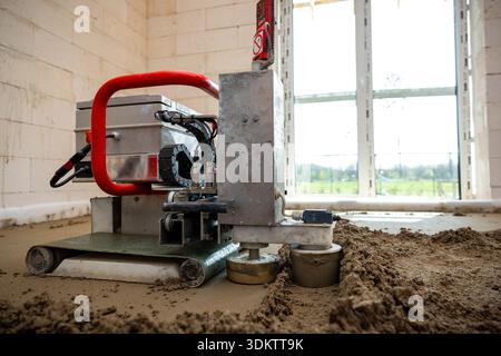 A construction site interior showing a machine with a red handle for underfloor heating pipe installation and Estrich concrete leveling on a lit concr Stock Photo