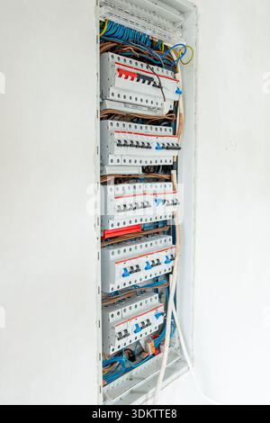 An open electrical panel in a white wall shows organized rows of circuit breakers and neatly arranged color coded wiring, including blue and yellow gr Stock Photo