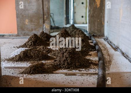 Construction site indoors showing soil piles on a white surface, a black pipe on the right, exposed concrete walls, and an open doorway in the backgro Stock Photo