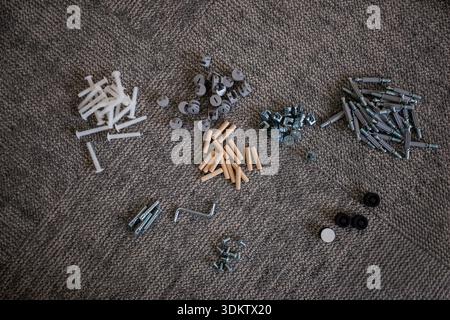 Neatly arranged hardware components including screws, nuts, bolts, dowels, pegs, caps, wheels, and a hex key on a textured gray surface. Stock Photo
