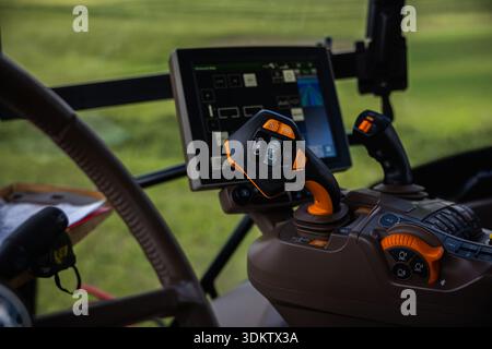 Close up of a tractor cab shows a joystick with orange accents, an auxiliary stick, and a touchscreen console running guidance and implement tools in Stock Photo
