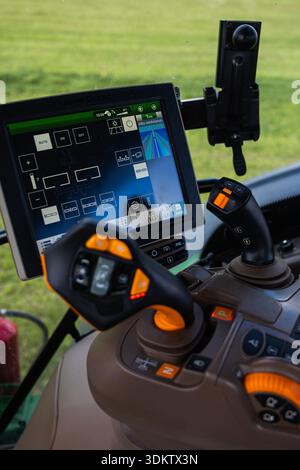 Close up of a John Deere tractor console shows dual joysticks, lit buttons, and a large touchscreen with rows guidance and hydraulic icons, indicating Stock Photo