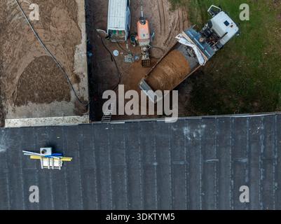 An aerial view of a construction site showing a dump truck unloading sand, a small excavator, a white utility van, tools, and materials on a roof. Stock Photo