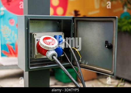 Open metal utility box shows IEC 60309 plug and blue sockets with thick cables. Droplets suggest recent rain. Title mentions open metal utility box. D Stock Photo