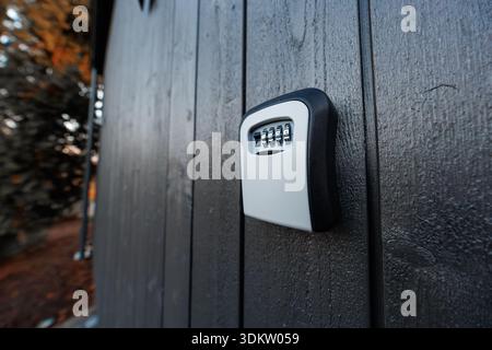 A mounted combination key safe with four dials sits on dark shed boards in cool evening light, shallow depth of field drawing focus to utilitarian des Stock Photo