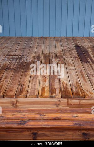A raised wooden deck shows damp patches and grain against blue cladding. Soft diffuse light suggests overcast shade, highlighting wear, knots, and mai Stock Photo