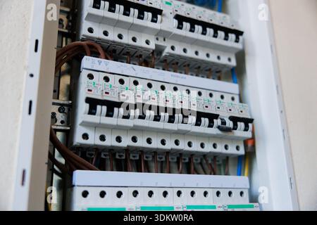Multiple rows of miniature circuit breakers show ON toggles, brown and blue conductors, DIN rail mounting, numbered terminals, and side lighting in an Stock Photo