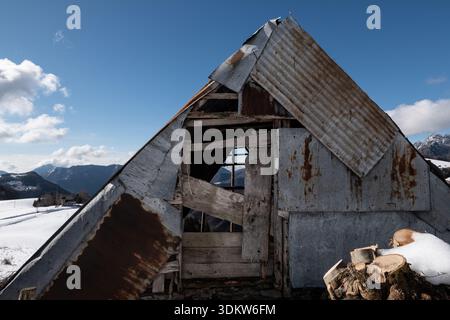 Abandoned rural mountain shelter built with wood and metal sheets standing in a snowy alpine landscape under clear winter light and blue sky. Cima Res Stock Photo
